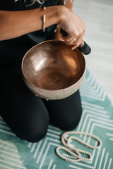 Close up image of woman’s hands holding Tibetan Singing Bowl indoors. The atmosphere of relaxation and Zen. Exercise for achieving clarity of mind and perfect body.