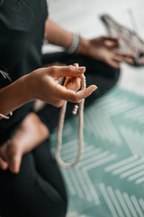 Young woman practicing yoga, sitting in Seated forward bend exercise and goes through the rosary , paschimottanasana pose, working out, wearing sportswear, indoor, home interior background, close up