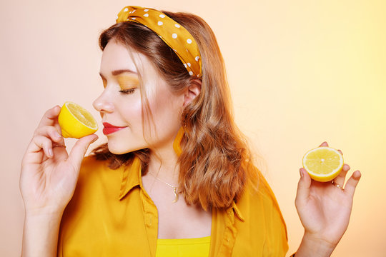 A beautiful portrait of a girl who eats a lemon, bites off a slice of lemon, a girl sniffs a lemon. Health, skin beauty, lemon-based face masks, lemon diet. Girl with bright  make-up.