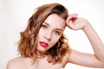 Fashion photo of a girl in golden accessories. Girl with professional golden make-up on a white background. A model with a short haircut in jewelry, earrings, many rings, earrings.