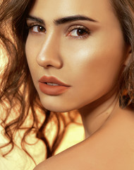 Fototapeta premium Portrait of a girl with professional skin treatment. Gold leather, magazine photo with fashionable tint. Portrait of an incredible brunette with professional brown make-up and curly hair. Nude lips.