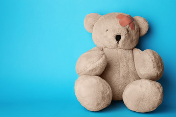 Toy teddy bear with sticking plasters on light blue background, space for text