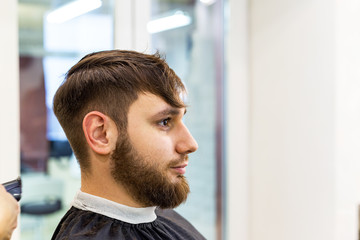 Hairdresser doing haircut for male client, man with beard using professional hairdresser tools, equipment on hairdresser work space, workplace. Hairdresser service.Barbershop hair cut, beard trimming.