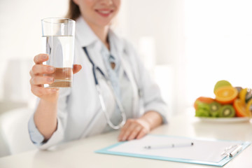 Nutritionist with glass of water at desk in office, closeup. Space for text