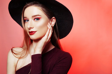 Gorgeous blonde in a big hat with burgundy make-up, red lips, and a burgundy dress. Girl in burgundy earrings, portrait of a model. Fashion photo of bright red makeup, model on a red background