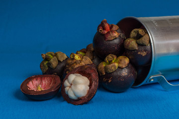 Mangosteen and cross section showing the thick purple skin and white flesh on blue background