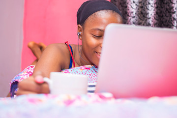 pretty african lady at home alone in her bedroom, watching a movie on her laptop pc