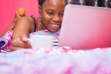 pretty african lady at home alone in her bedroom, watching a movie on her laptop pc