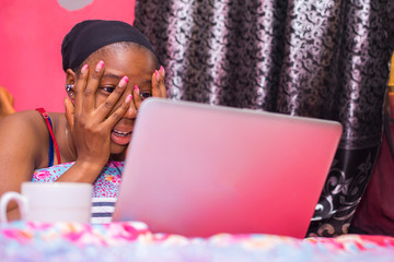 pretty african lady at home alone in her bedroom, watching a movie on her laptop pc looking scared...