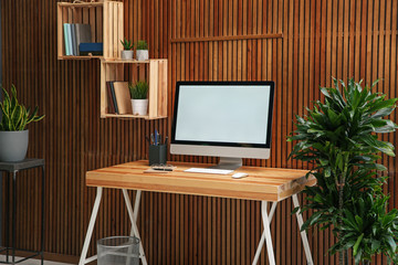 Comfortable workplace with computer near wooden wall in stylish room interior. Home office design