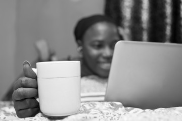 pretty african lady at home alone in her bedroom, watching a movie on her laptop pc, blurred, with...