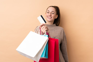 Young brunette woman over isolated background holding shopping bags and a credit card