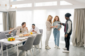 Group of young people spending time together in modern apartment at weekend, horizontal shot