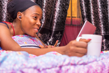 pretty african lady at home alone in her bedroom, watching a movie on her laptop pc