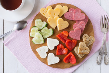 Valentine's day snack board with cheese, red pepper, sausage, bread, cucumber