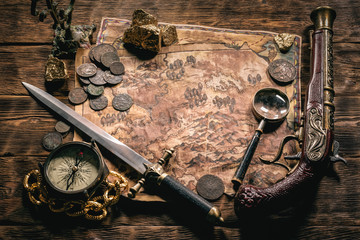 Pirate treasure map and other accessories on brown wooden table flat lay background.