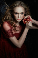Beautiful blonde girl with pomegranate fruit in her hands. Spring portrait of a girl in a red dress breaking a pomegranate, juice flowing down her hands
