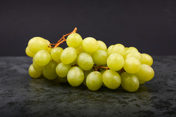 A bunch of green grape on a marble dark background. Volumetric winery. A bunch of green grape bush.