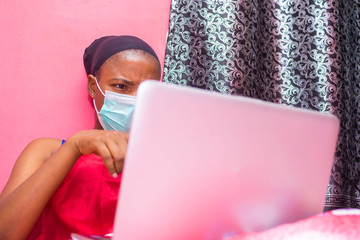 lady in her bedroom wearing a face mask using her laptop pc