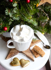 Obraz na płótnie Canvas Coffee in a white cup with marshmallows. Morning festive coffee with traditional Italian cantuccini almond cookies. A cup of coffee on a background of green fir branches on a white stand.