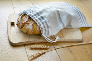 Tasty bread loaf in reusable zero waste linen bread bag on wooden cutting board