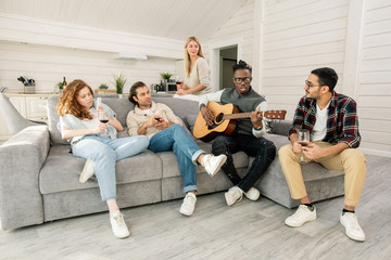 Horizontal shot of black guy playing guitar and singing song for his friends to listen to it