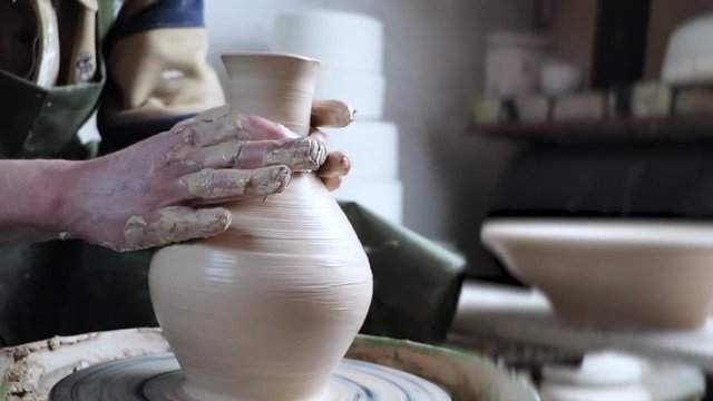 Hands of a potter on a pottery wheel close-up. Old traditional art, handmade, clay and ceramic production. Pottery workshop in subdued soft light