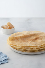 Crepes, thin pancakes with honey on a white plate. Marble background. Close up.