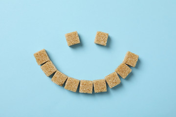 Smiley face made of sugar cubes on blue background, top view