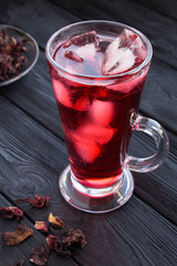 Iced hibiscus or karkade tea in the glass on the black wooden  background. Location vertical. Closeup.