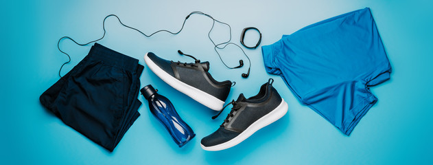 Flatlay blue clothing for running or crossfit, headphones, fitness bracelet, water bottle, shorts and t-shirt on a blue background