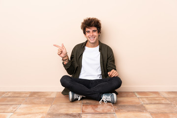 Young caucasian man sitting on the floor pointing finger to the side