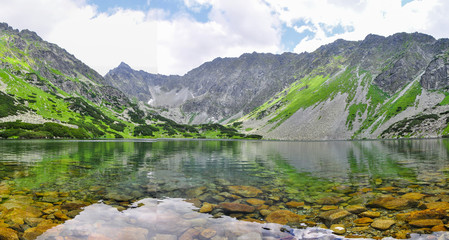 Naklejka na ściany i meble Glittering mountain lake. Lower Temnosmrečianske Lake. The lake surrounded by majestic and high cliffs. High Tatras national park, Slovakia. 