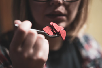 Woman pretending to eat red heart shape figures from the spoon. Selective focus. Valentine's day concept.