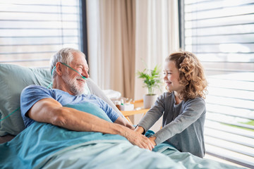 Small girl visiting ill grandfather in hospital room.