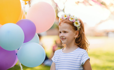 Small girl standing outdoors in garden, birthday celebration concept.