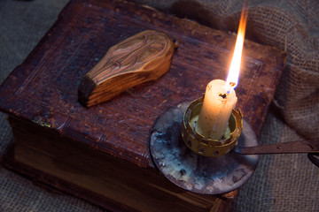Old book and rough cloth. A bright candle burns. The concept of occultism and magic. A wooden doll...