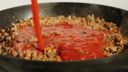 Tomato, bolognese sauce being added to ground or mince beef in black pan. Italian food concept