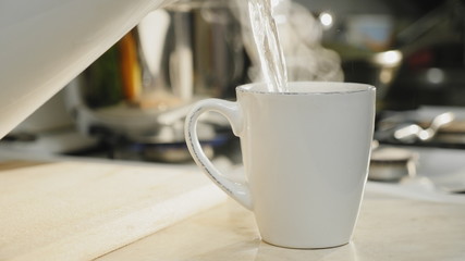 Close-up of hot boiled water is poured into a white ceramic cup on the table in the kitchen, brewing morning coffee