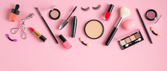 Frame top border of makeup products and cosmetics on pastel pink background. Flat lay, top view. Beauty blog banner template. Female make-up concept