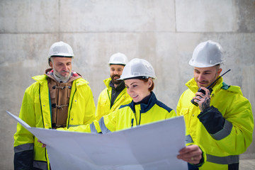 A group of engineers standing against concrete wall on construction site.