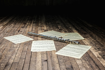 flute lies on a wooden stage among sheet music with notes © Chernobrovin