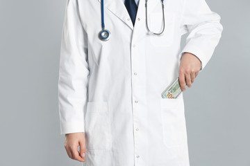 Doctor putting bribe into pocket on grey background, closeup. Corruption in medicine