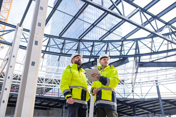 Men engineers standing outdoors on construction site, using tablet.