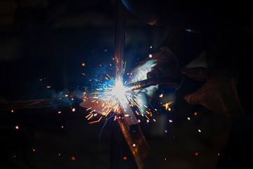 A welder is cooking metal in the dark. Great glow. Creating a design. Work in the workshop.