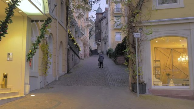 Calle solitaria de ciudad con anciana subiendo cuesta cansada