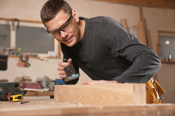 Professional carpenter grinding wooden plank with jack plane in workshop