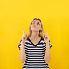 Joyful woman with gesture points fingers up and looking up on yellow background. Vertical banner with copy space