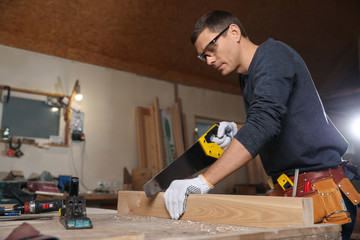 Professional carpenter sawing wooden plank at workbench