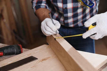 Professional carpenter measuring wooden plank at workbench, closeup